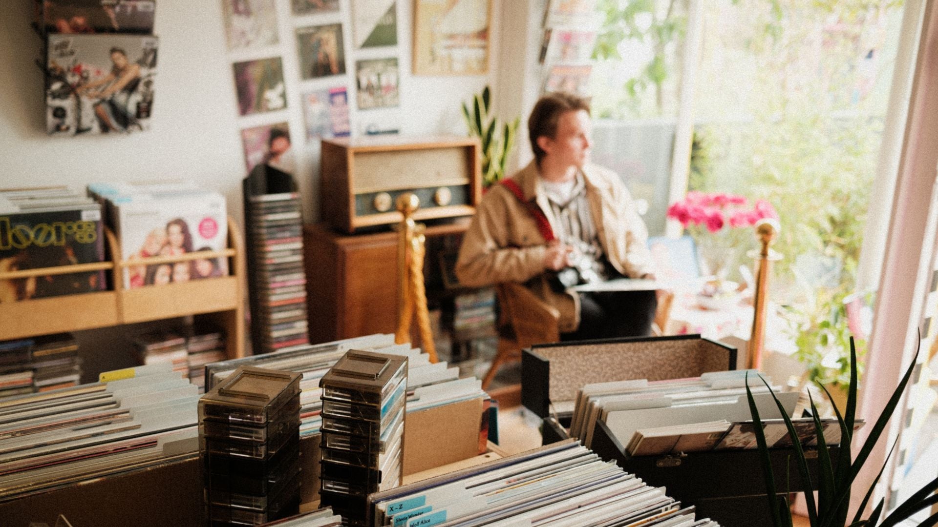Model Charlie Richards sits in a room filled with vinyl records, CDs, tapes and a vintage radio.